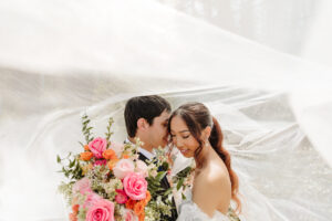 intimate wedding portrait with wedding couple embracing under veil in the sun